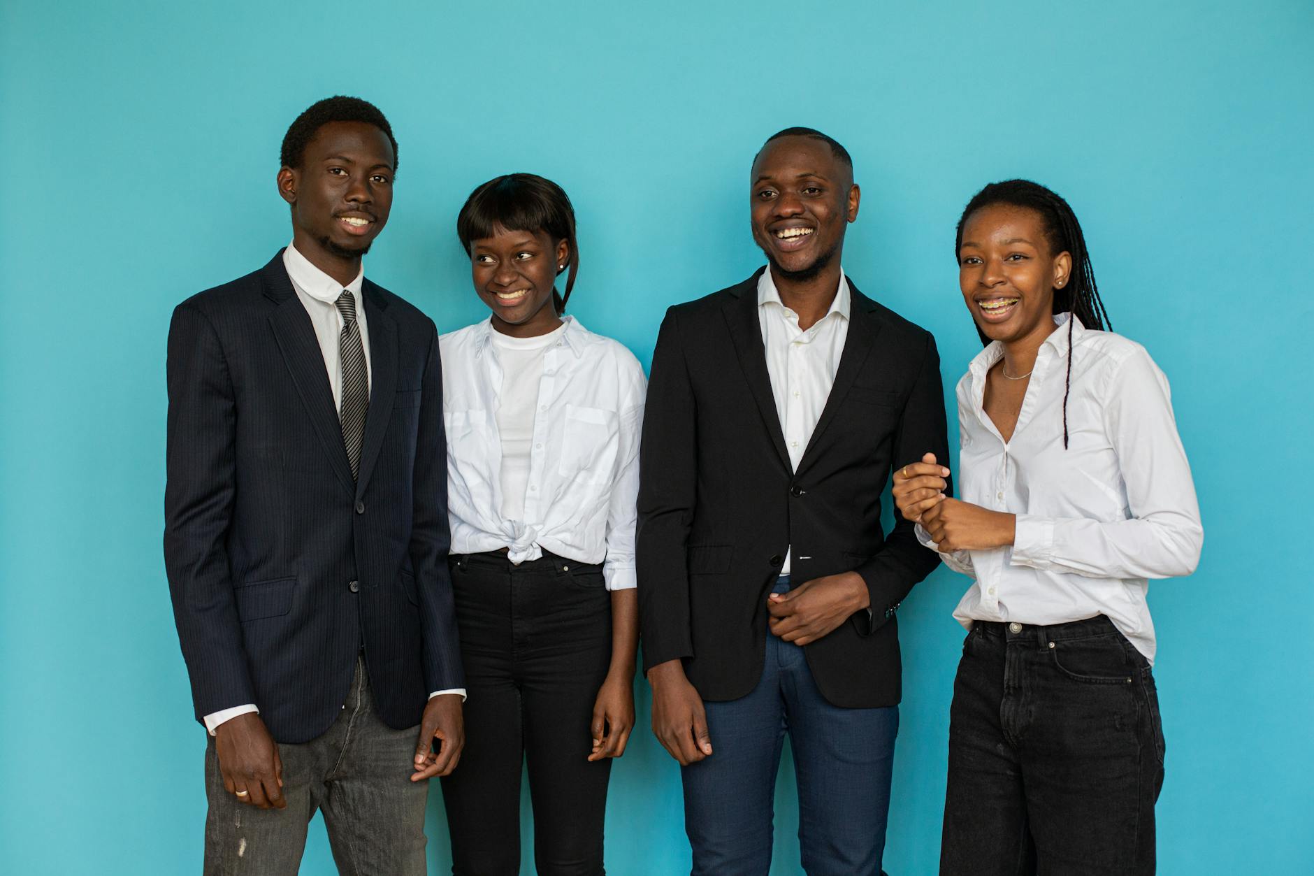 A group of smiling young professionals in a studio setting against a blue backdrop.